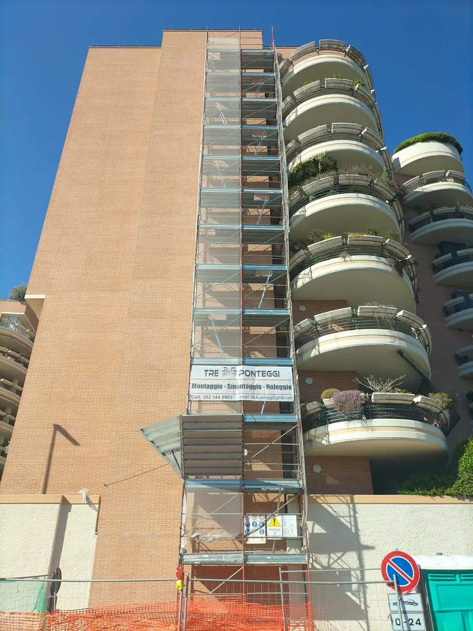 Ponteggio a torre lungo la facciata di un edificio alto con balconi curvi